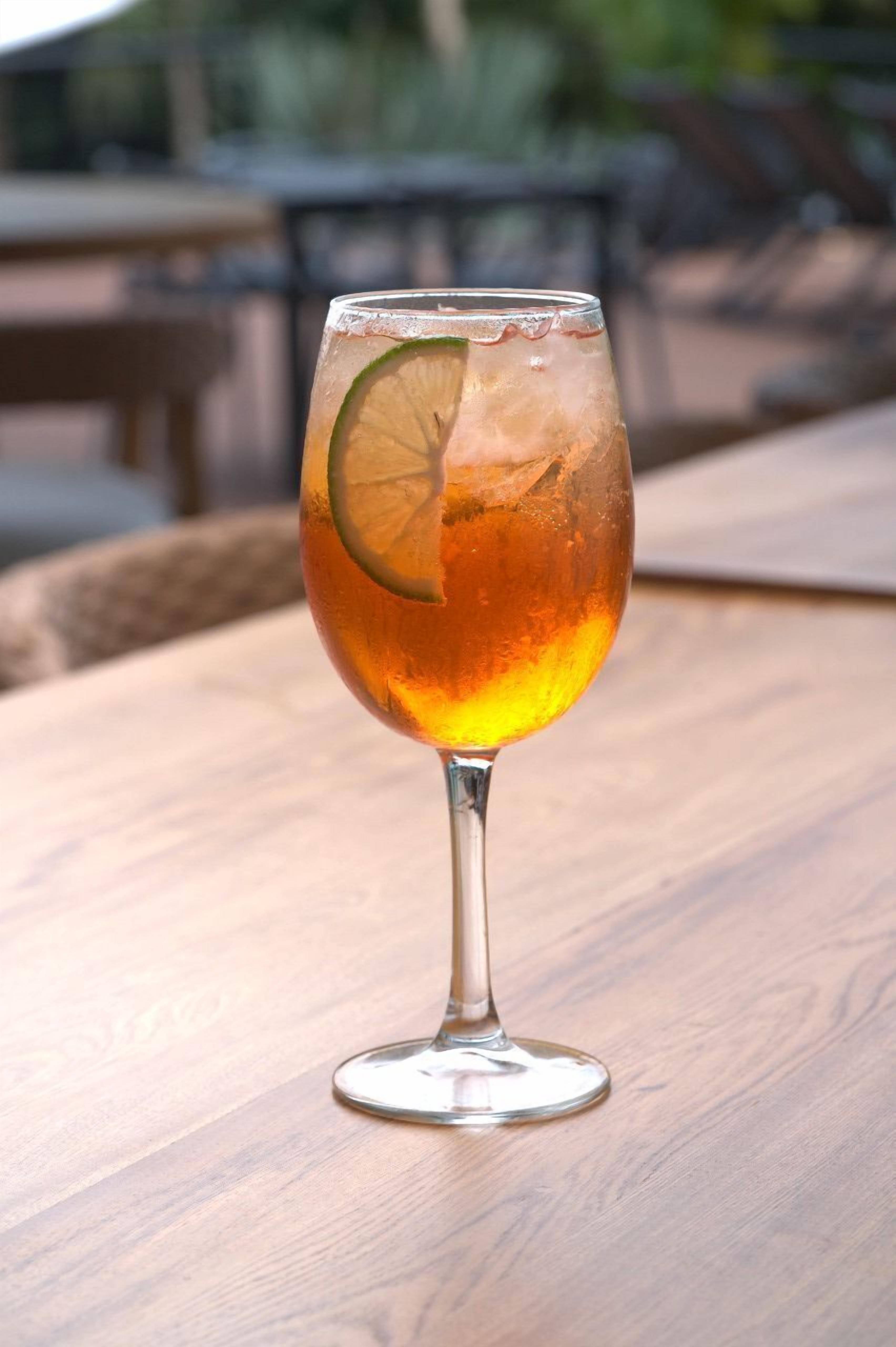 A glass of amber-colored beverage with a lime slice on a wooden table.