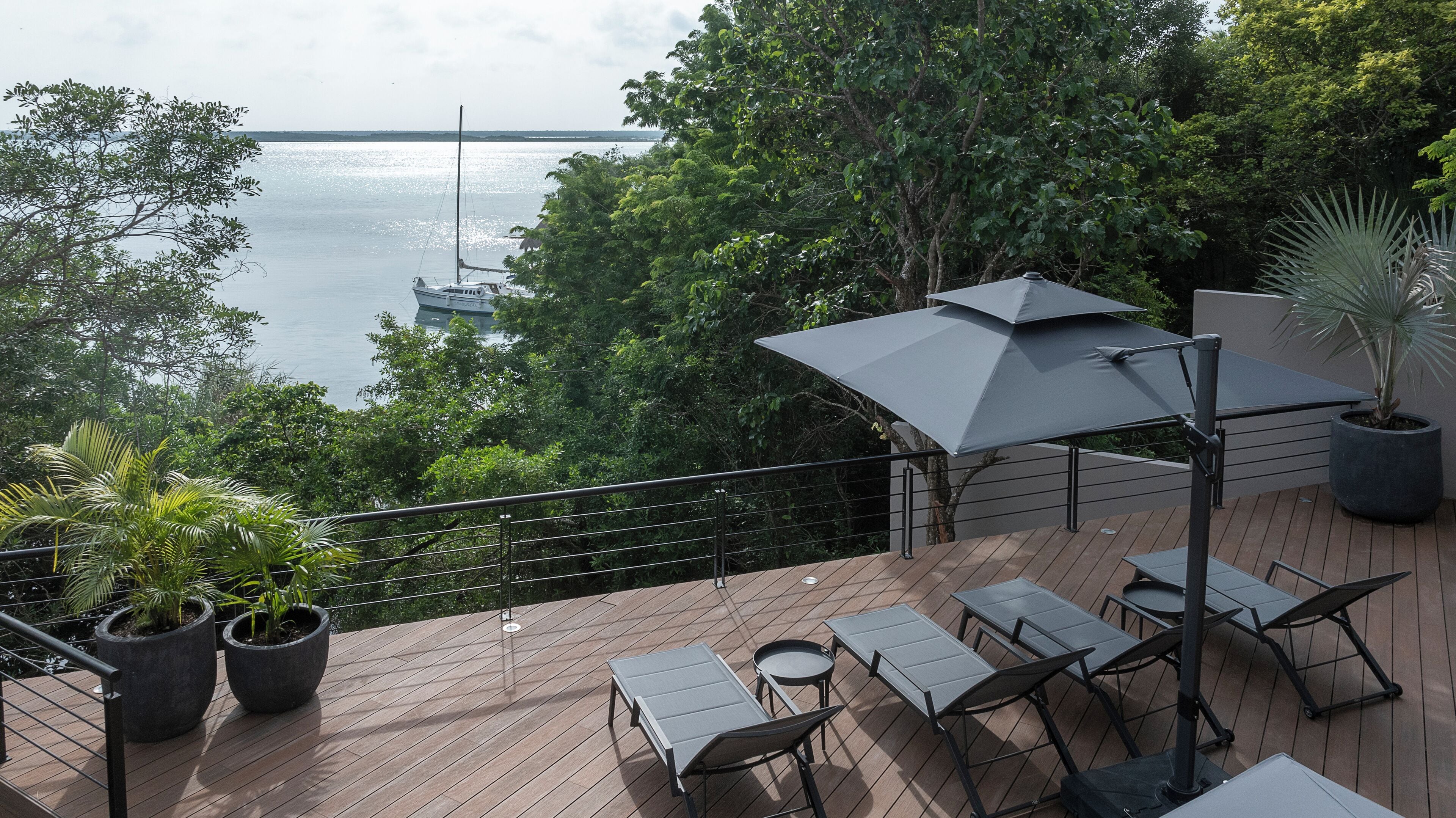 A deck with outdoor furniture, a large umbrella, and potted plants.