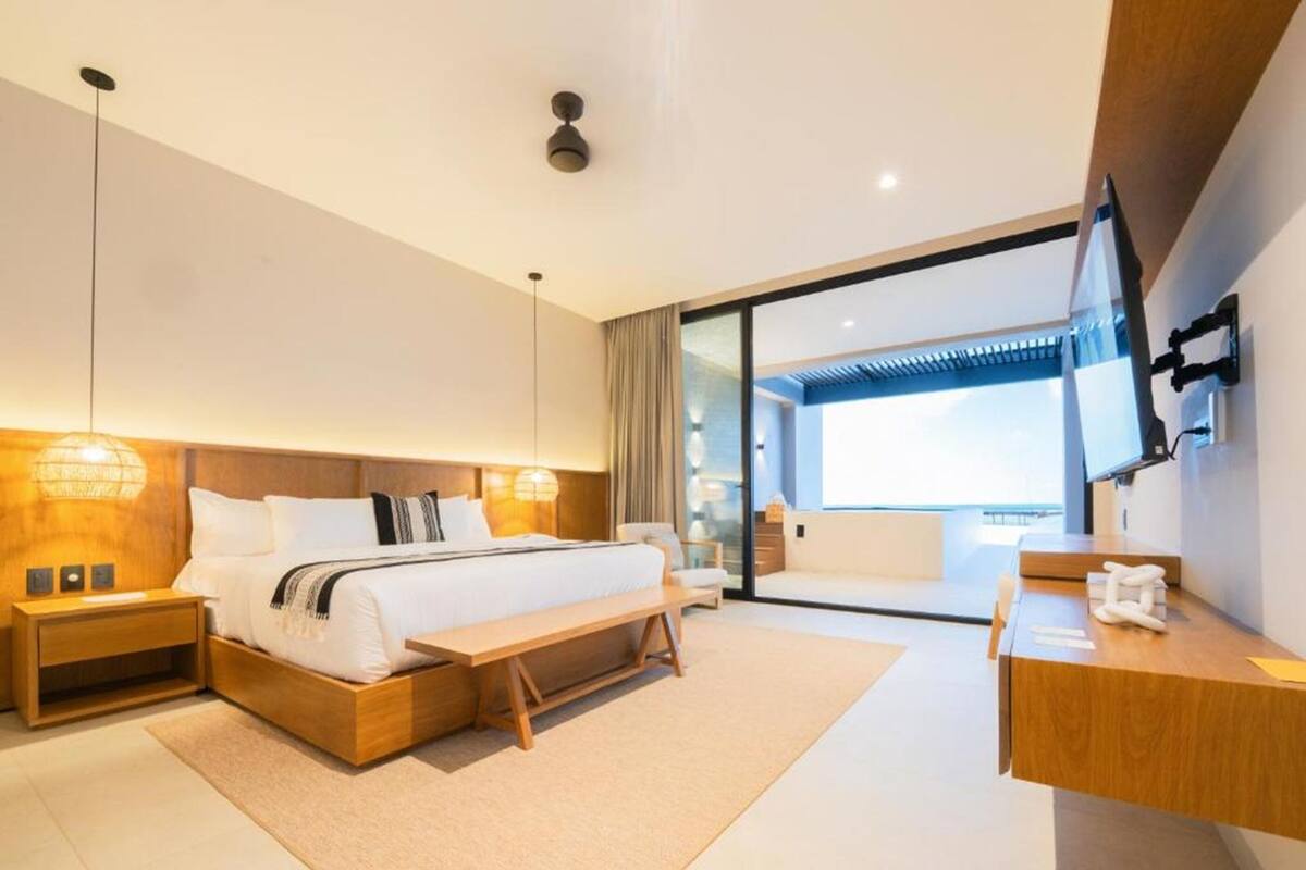 A modern hotel room with a large bed, bedside tables, a desk, and a large window.