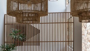 A modern interior with wicker pendant lights, a wooden slat partition, and two black chairs with patterned cushions. - Amaranto Hotel Boutique (Bacalar)