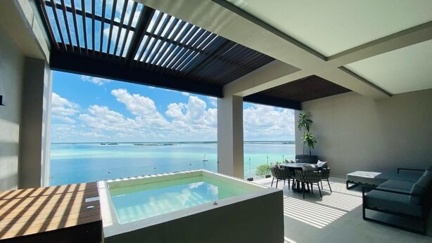 A modern outdoor living area with a hot tub, a dining table, and a sofa, overlooking a large body of water. - Amaranto Hotel Boutique (Bacalar)