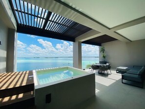 Een moderne buitenruimte met een hottub, een eettafel en een bank, met uitzicht op een groot wateroppervlak.