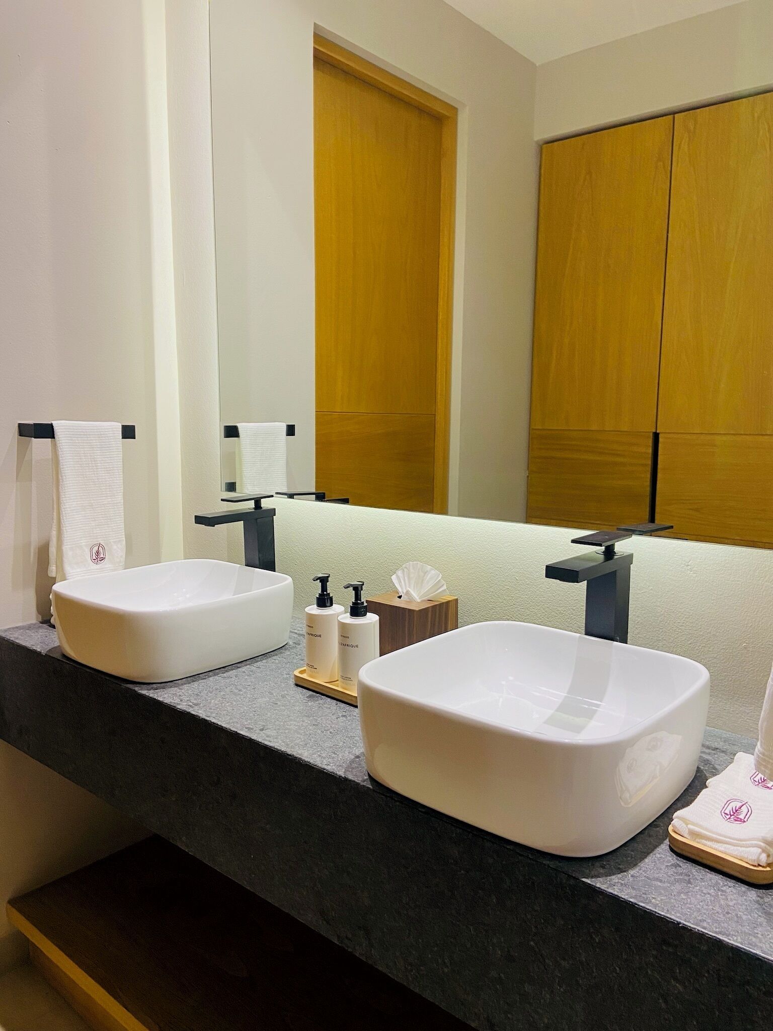 Baño con dos lavamanos, un espejo y una puerta de madera.