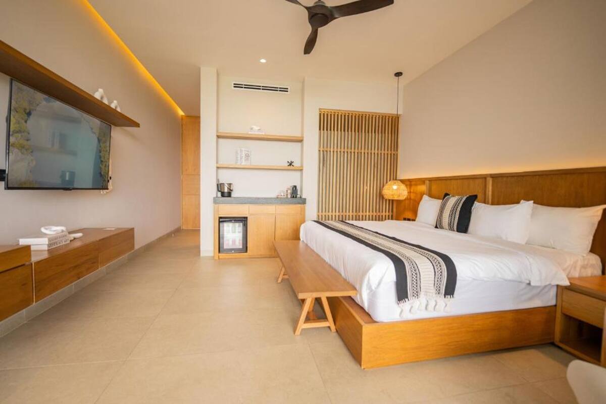 A modern bedroom with a bed, bench, bedside table, TV, and built-in shelving.