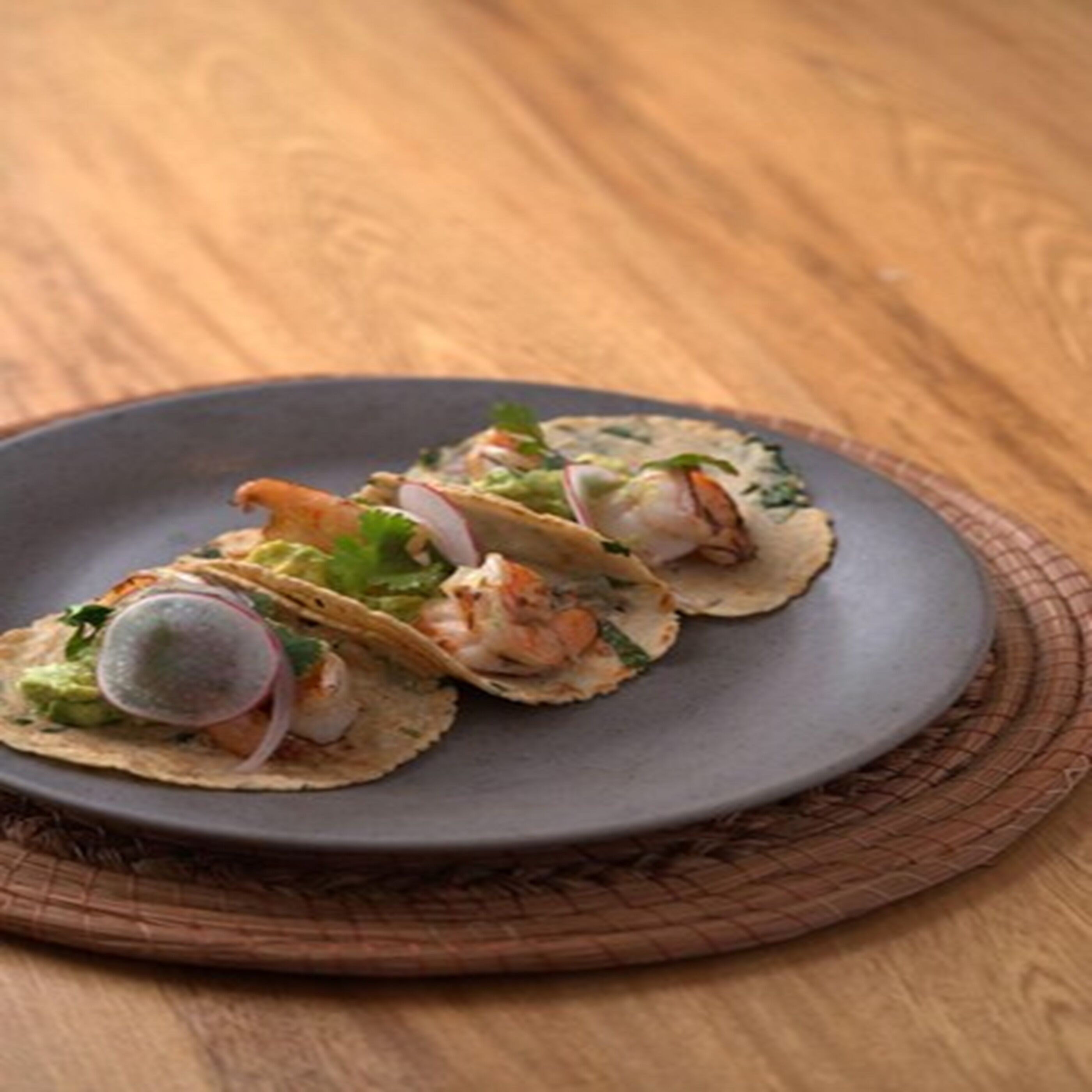 A plate of tacos with shrimp, avocado, and radish on a dark plate.