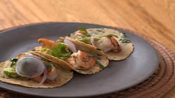 A plate of tacos with shrimp, avocado, and radish on a dark plate.