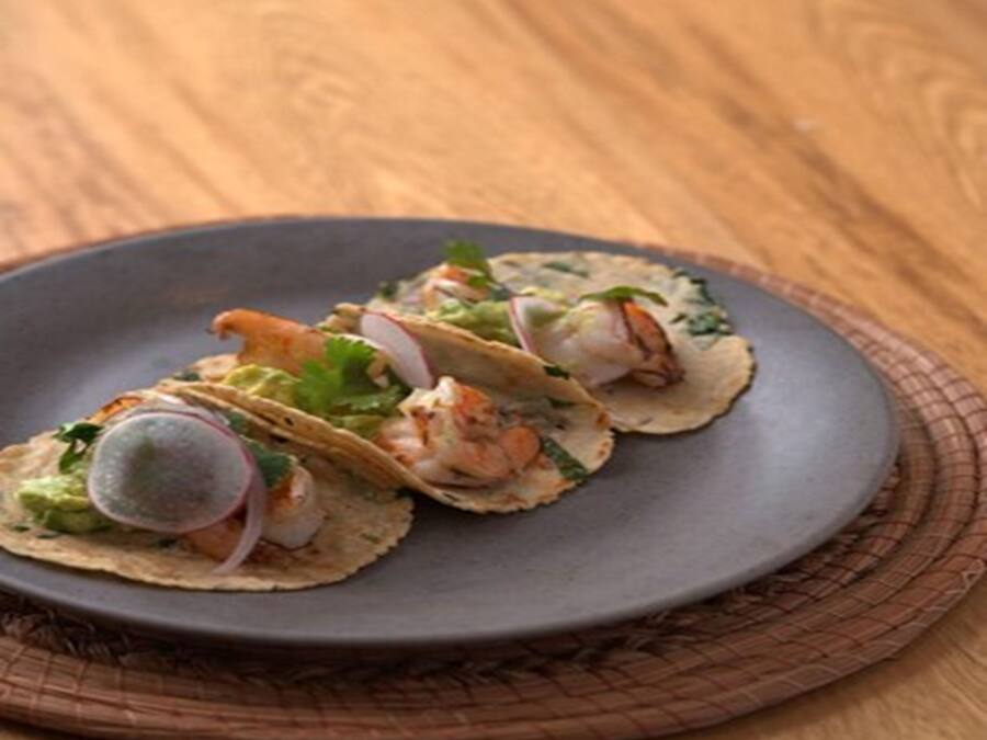 A plate of tacos with shrimp, avocado, and radish on a dark plate.