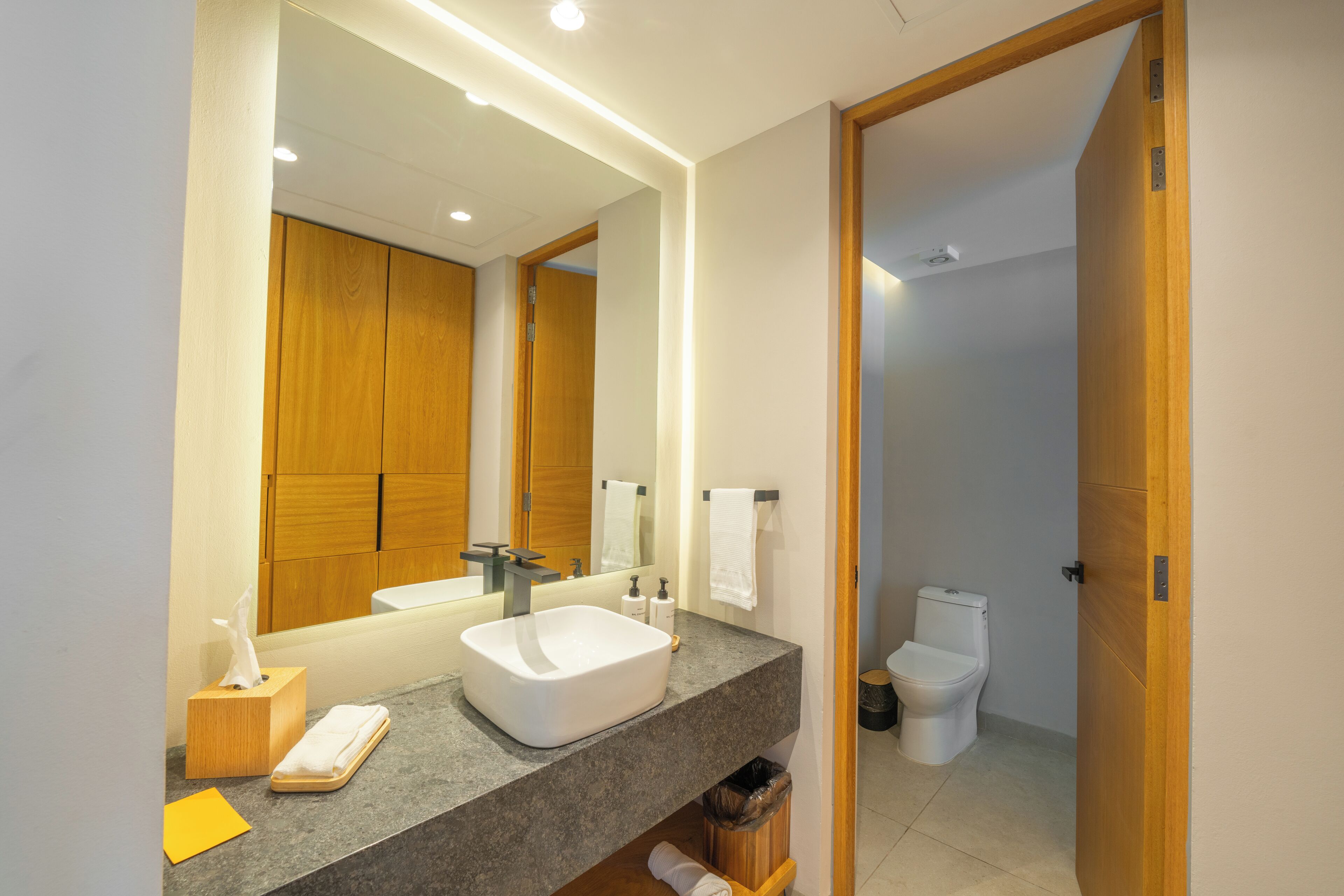 A modern bathroom with a large mirror, a white sink, and a wooden vanity.