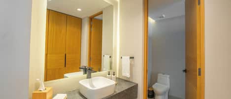 A modern bathroom with a large mirror, a white sink, and a wooden vanity.