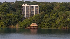 A modern building with multiple balconies overlooking a lake, surrounded by dense forest. - Amaranto Hotel Boutique (Bacalar)
