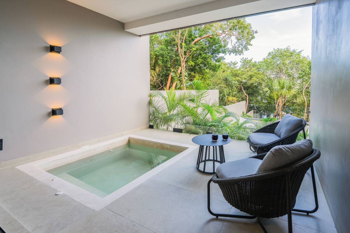 A modern outdoor area with a hot tub, two wicker chairs, and a small table with two glasses.