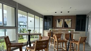 Un espace repas moderne avec des chaises en osier et une table ronde, de grandes fenêtres et une vue sur la verdure environnante.