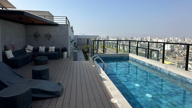 Un espace piscine sur le toit offrant une vue sur la ville, avec une terrasse en bois et des meubles de salon modernes.