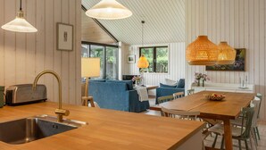A modern kitchen with wooden countertops, a stainless steel sink, and a built-in toaster. There is a dining area with a wooden table and chairs, and a blue sofa in the background. - 4 bedroom awesome home in Hornbæk (Hornbæk)