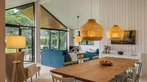 A spacious living room with a wooden dining table, blue sofas, and large windows offering a view of greenery. - 4 bedroom awesome home in Hornbæk (Hornbæk)