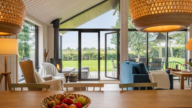 A cozy living room with a large window, a fireplace, and a dining area with a table and chairs. - 4 bedroom awesome home in Hornbæk (Hornbæk)