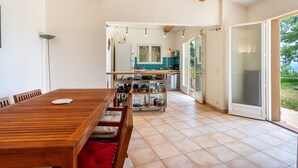 Un grand espace à manger avec une table et des chaises en bois, une cuisine à l’arrière-plan et une porte-fenêtre coulissante donnant sur un espace extérieur.