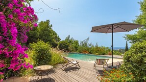 Une terrasse en bois avec une piscine, entourée d’une végétation luxuriante et de fleurs aux couleurs vives.