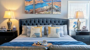 A bedroom with a large bed, two bedside tables, a window with blinds, and a painting of a coastal landscape. - Big house w custom murals/2 Kings/Fun backyard w Games/Grill/Dog OK/Boat parking (Page)