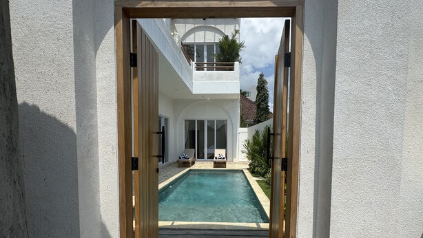 A view through a doorway into a modern house with a swimming pool, a balcony, and a patio area. - Villa Amici (Canggu)