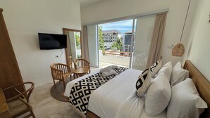 A hotel room with a bed, a TV, a balcony with a view of buildings, and a wooden chair. - Villa Amici (Canggu)