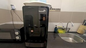 Uma cafeteira com reservatório de água e painel de controle, uma pia e uma torneira em uma cozinha.