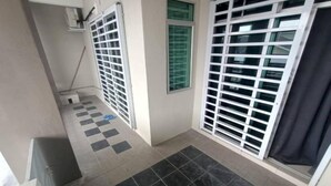 Um corredor com chão xadrez, um esfregão encostado na parede e uma janela com grade de metal.