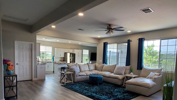 A spacious living area with a large sofa, a coffee table, and a blue rug. There is a kitchen in the background with white cabinets and a dining area. - Completely Remodeled and Modernized Smart Home in Payson (Payson)