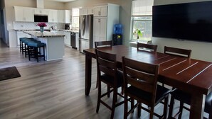 A modern kitchen with white cabinets, a central island, and a dining area with a wooden table and chairs. - Completely Remodeled and Modernized Smart Home in Payson (Payson)