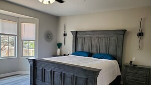 A bedroom with a large bed, a nightstand, a dresser, a wall clock, and a window with blinds. - Completely Remodeled and Modernized Smart Home in Payson (Payson)