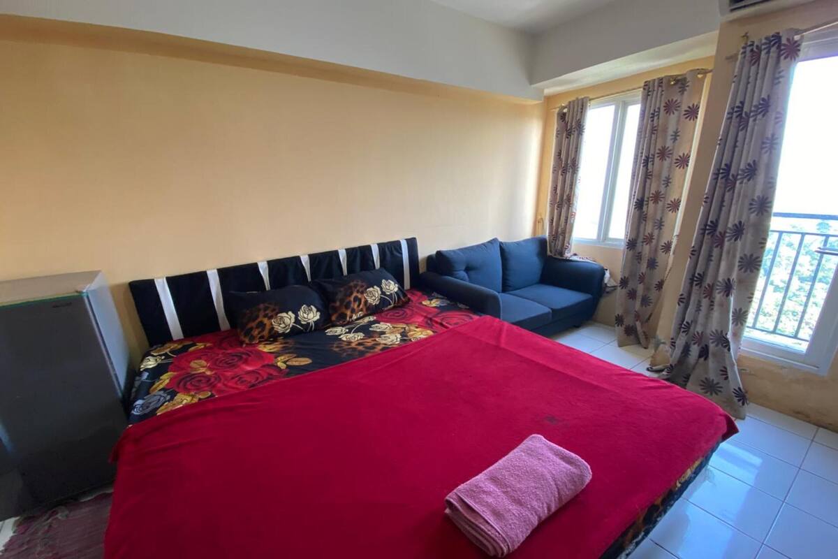 Quarto com cama, sofá, televisão e varanda com cortinas.