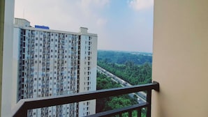 Un edificio de gran altura con varios balcones, vistas despejadas a una autopista y abundante vegetación al fondo.