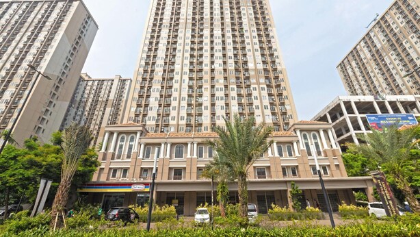 Un edificio residencial de gran altura con varios balcones, una entrada central con marquesina y zonas verdes circundantes.
