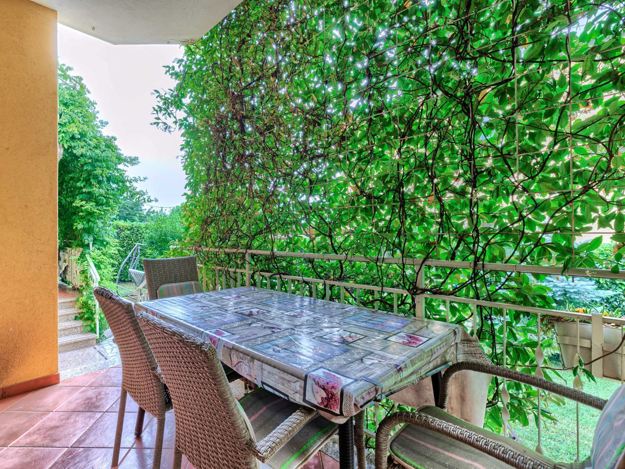 Eine Terrasse im Freien mit Tisch und Stühlen, umgeben von üppigem Grün und einem weißen Geländer.