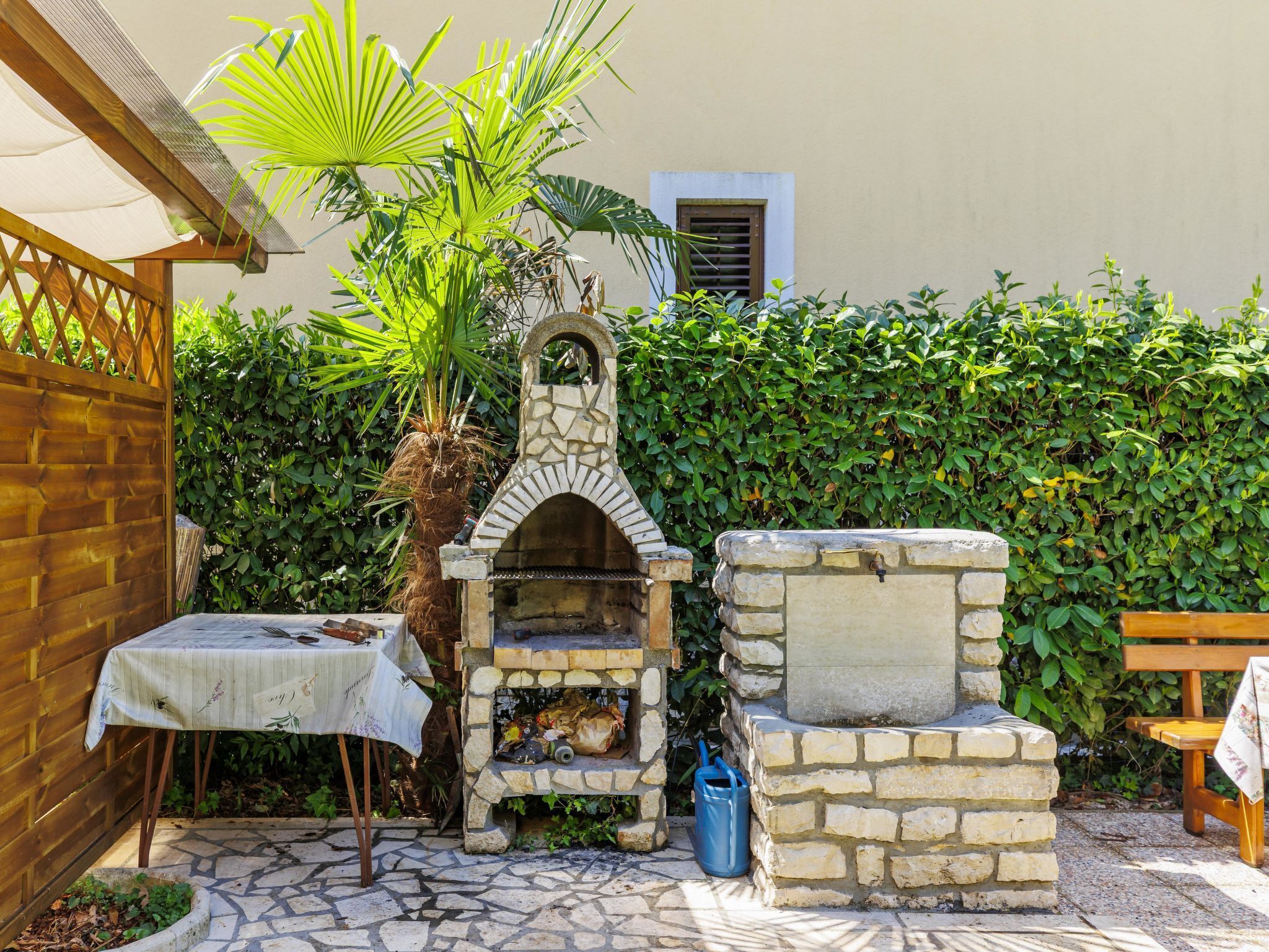 A stone-built outdoor oven with a chimney, a table with a cloth, and a bench.