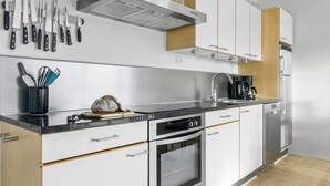 A modern kitchen with stainless steel appliances, a bread loaf on the counter, and a variety of knives hanging above the sink. - Gudhjem Søpark Lejl. 26 (Gudhjem)
