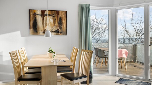 A dining area with a wooden table and chairs, a pendant light, and a painting on the wall. - Gudhjem Søpark Lejl. 26 (Gudhjem)