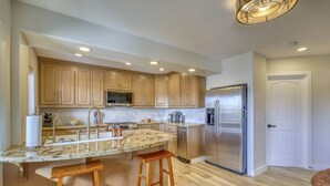 A kitchen with wooden cabinets, a stainless steel refrigerator, a granite countertop, and two wooden stools. - Lakefront, Fireplace, Large Deck, Yard & Dock. Mins from Uptown Dining & Trails! (Pagosa Springs)