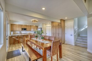 Una cocina amplia con armarios de madera, una mesa de comedor con bancos, y una escalera que conduce a un nivel superior.