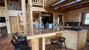Ein rustikales Holzhäuschen im Inneren mit Küchenbereich, einem Essbereich mit Hockern und einer Treppe zu einem Schlafboden.