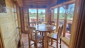 Ein Essbereich mit Holzboden, einem runden Tisch und Stühlen, großen Fenstern und Blick ins Freie.