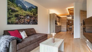 A modern living room with a brown sofa, a coffee table, and a large mountain landscape painting on the wall. - Beautiful apartment with a sauna and a balcony (Haus im Ennstal)
