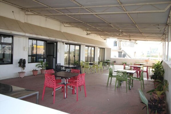 Un espace extérieur aménagé en terrasse, avec des tables et des chaises, des plantes en pot et un toit abrité.