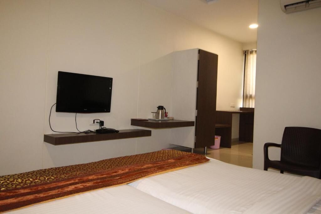 Una camera d'hotel con un letto, una TV a muro, una scrivania con una sedia e un angolo cottura.