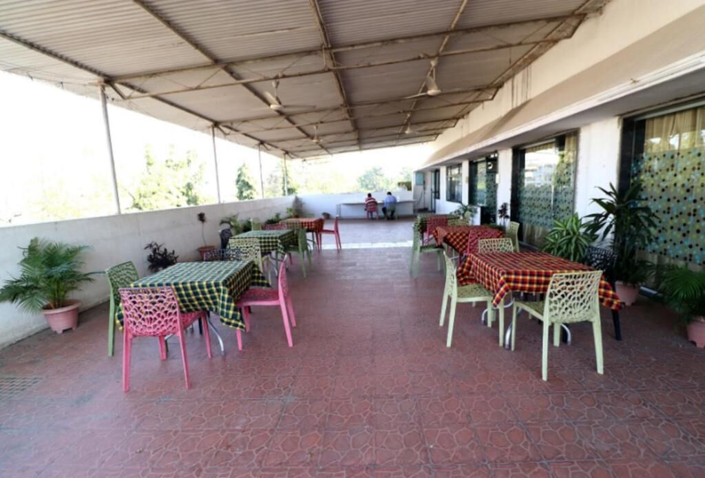 An outdoor patio area with tables and chairs, covered by a metal roof, and potted plants around.