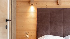 A bedroom with a wooden headboard, a bedside table with a vase, and a bed with white bedding. - Atmospheric with a sunny balcony and summercard (Haus im Ennstal)