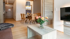 A modern living room with a wooden floor, a TV, a dining area with wooden chairs, and a vase with flowers. - Atmospheric with a sunny balcony and summercard (Haus im Ennstal)