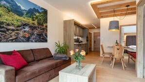 A modern living room with a brown sofa, a wooden coffee table, and a painting of a mountain landscape. - Atmospheric with a sunny balcony and summercard (Haus im Ennstal)