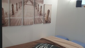 A bedroom with a bed, a pillow, and three wall-mounted pictures depicting a wooden pier with figures. - Le Petit Jules (Agen)