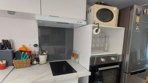 A modern kitchen with white cabinetry, a built-in oven, a stainless steel refrigerator, and a microwave. - Le Petit Jules (Agen)
